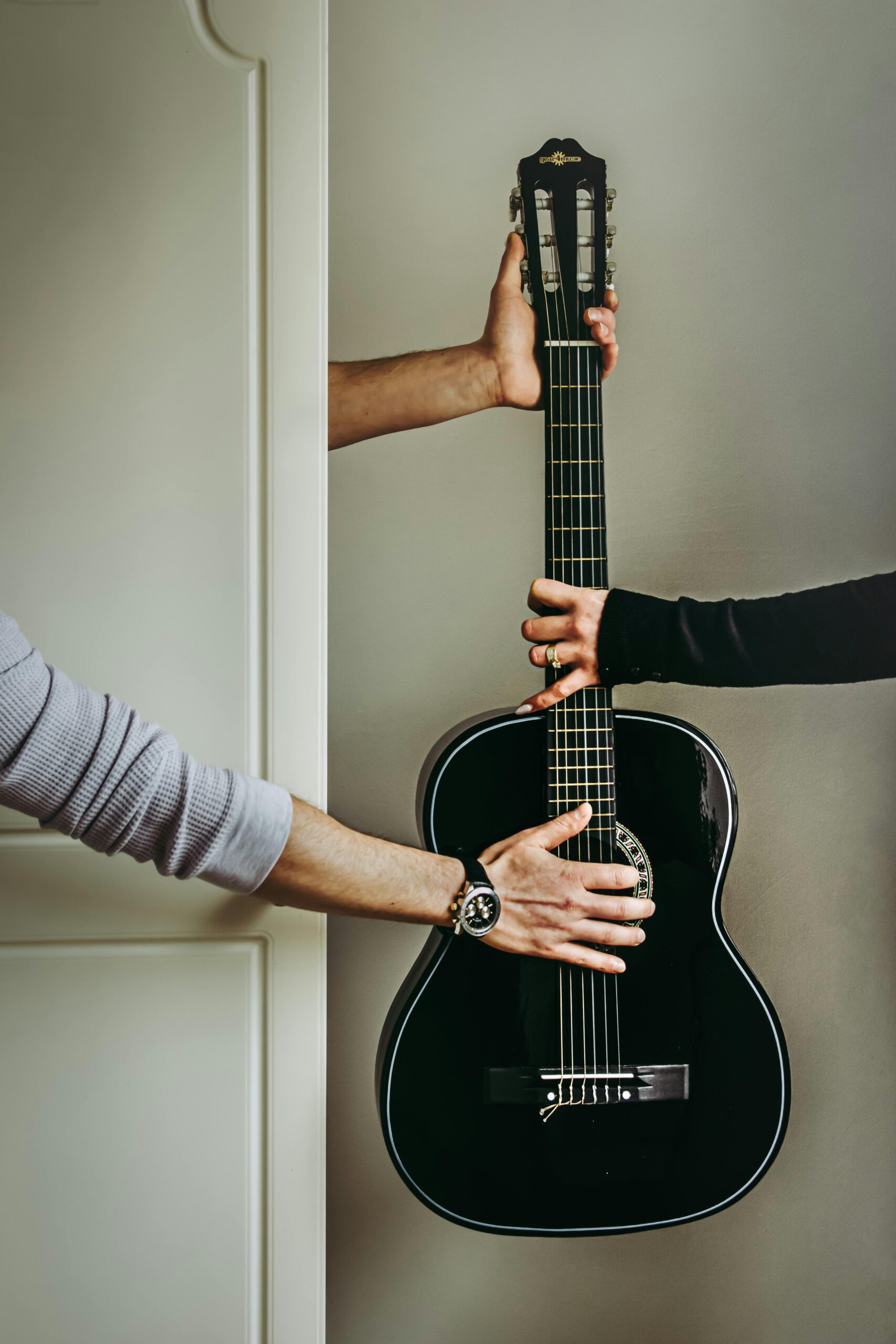 Three diverse hands holding an acoustic guitar, representing the universal passion for music and VibrArt Design's commitment to instrument care.